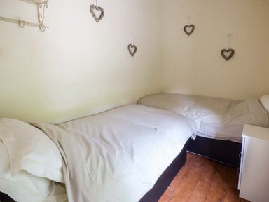 A small bedroom with two single beds covered in white bedding and heart-shaped decorations on the walls at Ploony Cottage in Bleddfa