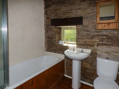 A bathroom with a bathtub sink and toilet against a stone wall at Ploony Cottage in Bleddfa