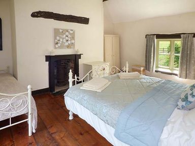 A bedroom with two beds a fireplace a window with curtains and wooden flooring at Ploony Cottage in Bleddfa