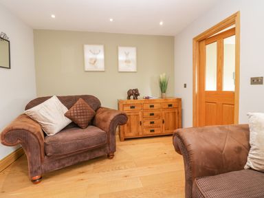 A sitting room with two brown armchairs a wooden cabinet with decorations and two framed animal pictures at Primrose Cottage in Aldingham
