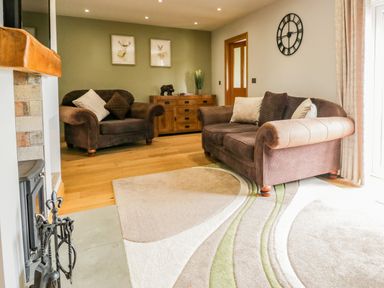 A living room with two brown sofas a wooden cabinet wall clock and a fireplace at Primrose Cottage in Aldingham
