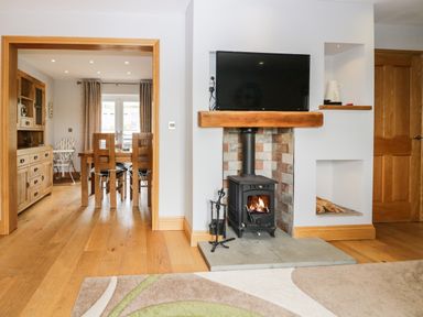 A living room with a wood burning stove and television with a view into a dining room with wooden furniture at Primrose Cottage in Aldingham