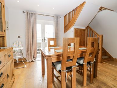 A dining area with a wooden table and chairs near stairs and glass doors with curtains at Primrose Cottage in Aldingham