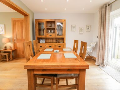A dining room with a wooden dining table and chairs a wooden cabinet and a high chair at Primrose Cottage in Aldingham