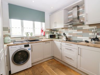 A kitchen with a washing machine sink microwave stovetop and utensils at Primrose Cottage in Aldingham
