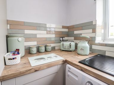A kitchen corner with a toaster kettle storage jars and a washing machine at Primrose Cottage in Aldingham