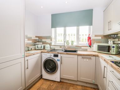A kitchen with a washing machine under the counter a sink under a window a toaster kettle and microwave on the counters at Primrose Cottage in Aldingham
