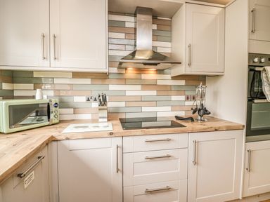 A kitchen with white cabinets a wooden countertop a microwave stove and an oven at Primrose Cottage in Aldingham
