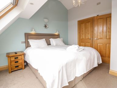 A bedroom with a bed and white linens next to a wooden nightstand and wooden doors at Primrose Cottage in Aldingham