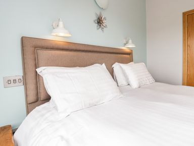 A bed with white pillows and bedding with a beige headboard and wall lights in a bedroom