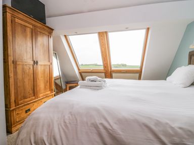 A bedroom with a large bed, wooden wardrobe, mirror, and windows showing a green landscape at Primrose Cottage in Aldingham