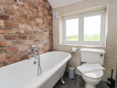 A bathroom with a clawfoot bathtub and a toilet under a window at Primrose Cottage in Aldingham