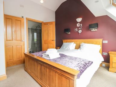 A bedroom with a wooden bed, white bedding, folded towels, wooden doors, and an en suite bathroom at Primrose Cottage in Aldingham