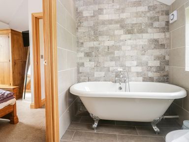 A bathroom with a freestanding bathtub and tiled walls next to a bedroom visible through a wooden door at Primrose Cottage in Aldingham