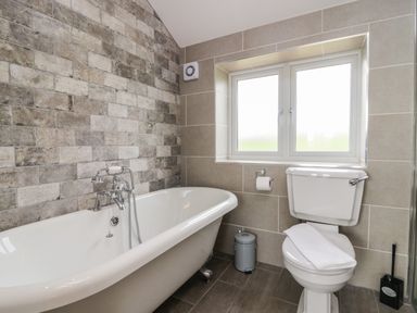 A bathroom with a bathtub toilet trash bin and window at Primrose Cottage in Aldingham