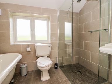 A bathroom with a toilet, a bathtub, a shower with glass panels, and a window at Primrose Cottage in Aldingham