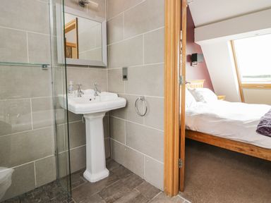 A bathroom with a pedestal sink and mirror next to a bedroom with a bed and window at Primrose Cottage in Aldingham