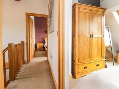A hallway leading to a bedroom with wooden furniture including a wardrobe and bedside table at Primrose Cottage in Aldingham