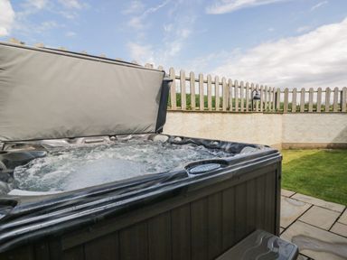 An outdoor hot tub with bubbling water next to a stone patio and a grass lawn at Primrose Cottage in Aldingham