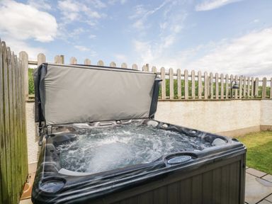 A bubbling hot tub with a partially opened cover in an outdoor fenced area at Primrose Cottage in Aldingham