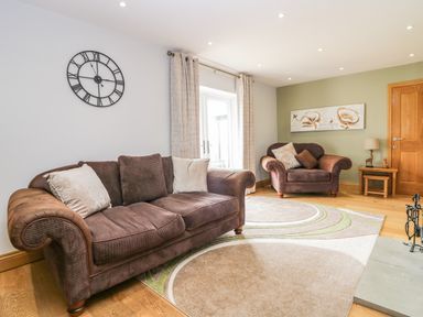 A living room with two brown sofas a wall clock on a white wall a wooden door and a large wall painting at Primrose Cottage in Aldingham