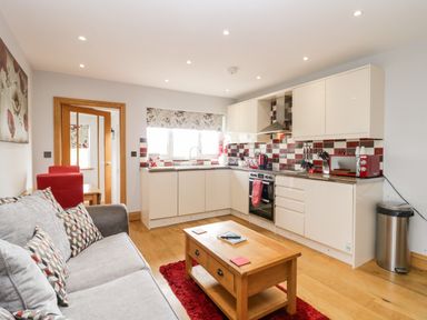 A kitchen and living area with a gray sofa a wooden coffee table and red accents at Daisy Cottage in Aldingham