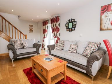A living room with two sofas a wooden coffee table a red rug and patterned curtains at Daisy Cottage in Aldingham