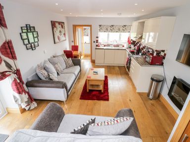 An open plan living room and kitchen area with sofas and a wooden coffee table at Daisy Cottage in Aldingham