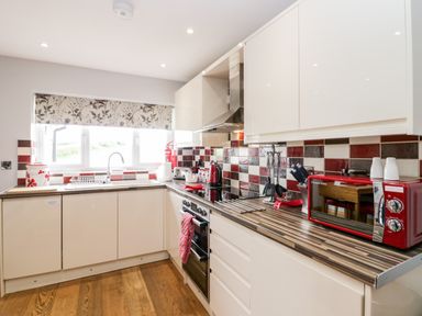 A kitchen with white cabinets red and black tiled backsplash and wooden floor at Daisy Cottage in Aldingham