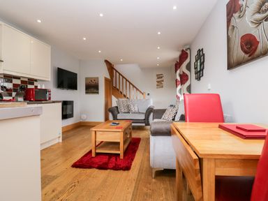 A living room with a wooden coffee table on a red rug and a grey sofa with patterned cushions at Daisy Cottage in Aldingham