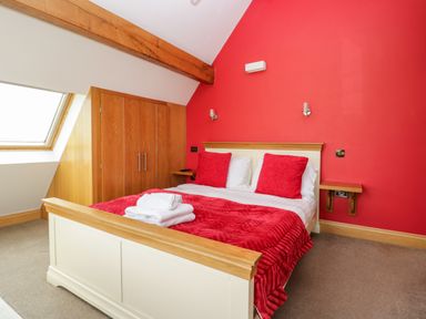 A bedroom with a double bed with red pillows and blanket a wooden wardrobe and a skylight at Daisy Cottage in Aldingham