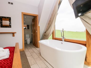 A bedroom with a freestanding bathtub next to a large window and an adjoining bathroom at Daisy Cottage in Aldingham