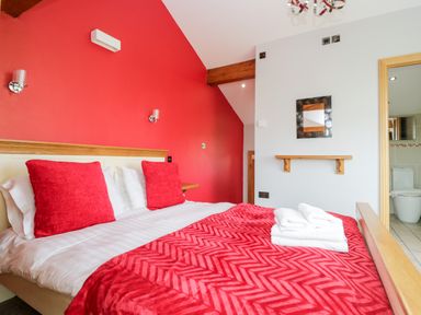 A bedroom with a bed with red pillows and blanket and white towels on the bed at Daisy Cottage in Aldingham