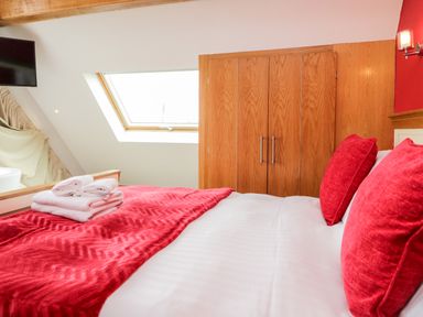 A bedroom with a bed with red pillows and blanket a wooden wardrobe and a skylight window at Daisy Cottage in Aldingham