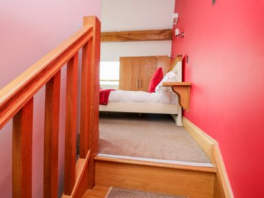 A staircase leading up to a bedroom with a bed and wooden wardrobe at Daisy Cottage in Aldingham