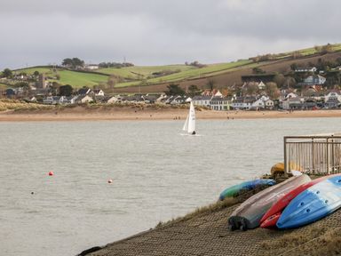 A riverside view with kayaks on the shore and a sailboat on the water and houses and green hills in the background at Pound Cottage in Huntshaw near Great Torrington
