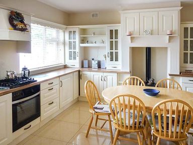 A kitchen with white cabinets wooden countertops a stove an oven a round wooden table six wooden chairs and a blue bowl on the table at Lovers Lodge in Kilkenny County Kilkenny