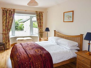 A bedroom with a wooden bed white bedding a red blanket two bedside tables with lamps and a window with curtains at Lovers Lodge in Kilkenny County Kilkenny