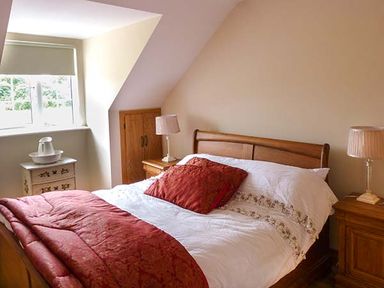 A bedroom with a wooden bed and red bedding a chest of drawers with a basin and jug two bedside tables with lamps at Lovers Lodge in Kilkenny County Kilkenny