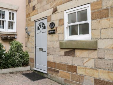 A stone exterior wall with a white door and window next to some plants at Razorbill Cottage in Whitby