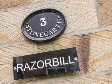 A stone wall with a black oval plaque showing number 3 and word Stonegarth and a black rectangular sign with the word Razorbill