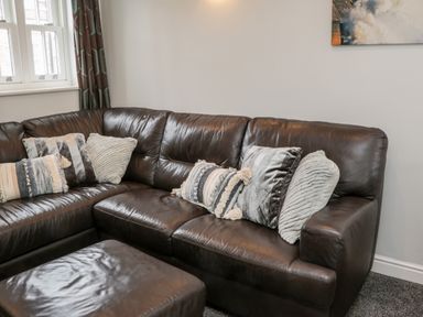 A corner of a living room with a dark brown leather sectional sofa and several textured pillows at Razorbill Cottage Whitby
