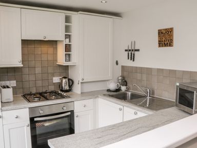 A kitchen with white cabinets a gas stove oven a sink microwave and a kettle at Razorbill Cottage Whitby