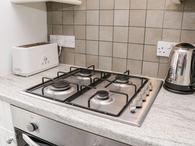 A kitchen countertop with a gas stove a white toaster and a stainless steel kettle at Razorbill Cottage in Whitby