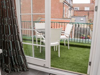 A balcony with a table and three white chairs and green artificial grass visible through sliding glass doors at Razorbill Cottage in Whitby