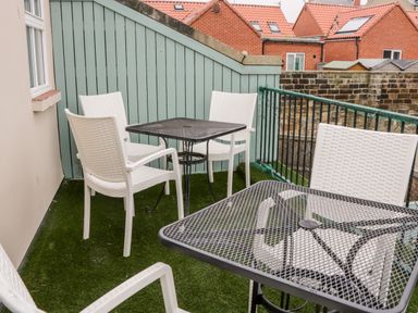A balcony with two black metal tables and six white chairs with artificial grass flooring at Razorbill Cottage in Whitby