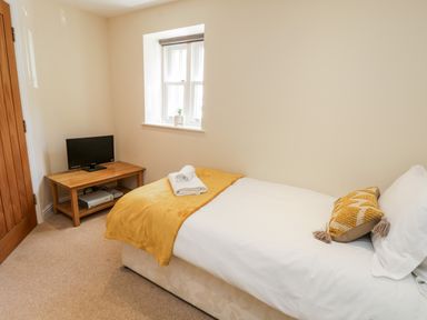 A small bedroom with a single bed next to a window and a wooden table with a TV at Razorbill Cottage Whitby
