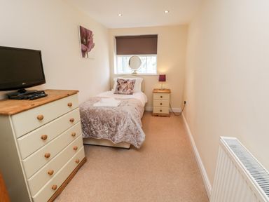 A bedroom with a single bed a chest of drawers with a TV and a bedside table with a lamp at Razorbill Cottage in Whitby