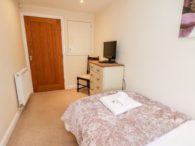 A bedroom with a bed covered with folded towels a chest of drawers a chair a small wall cabinet a wooden door and a wall radiator at Razorbill Cottage Whitby