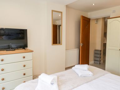 A bedroom with a bed and folded towels a chest of drawers with a television a mirror on the wall and an open door to an adjoining room at Razorbill Cottage Whitby